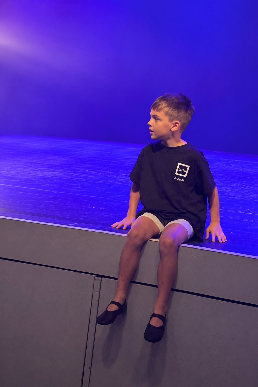Edward sitting on the edge of the stage under purple lighting